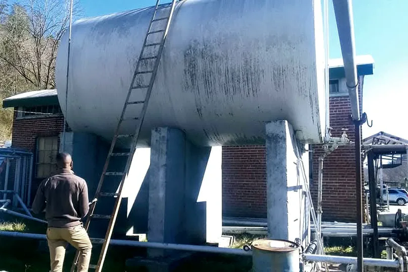 Representative inspecting an elevated storage tank on concrete piers at a fuel facility