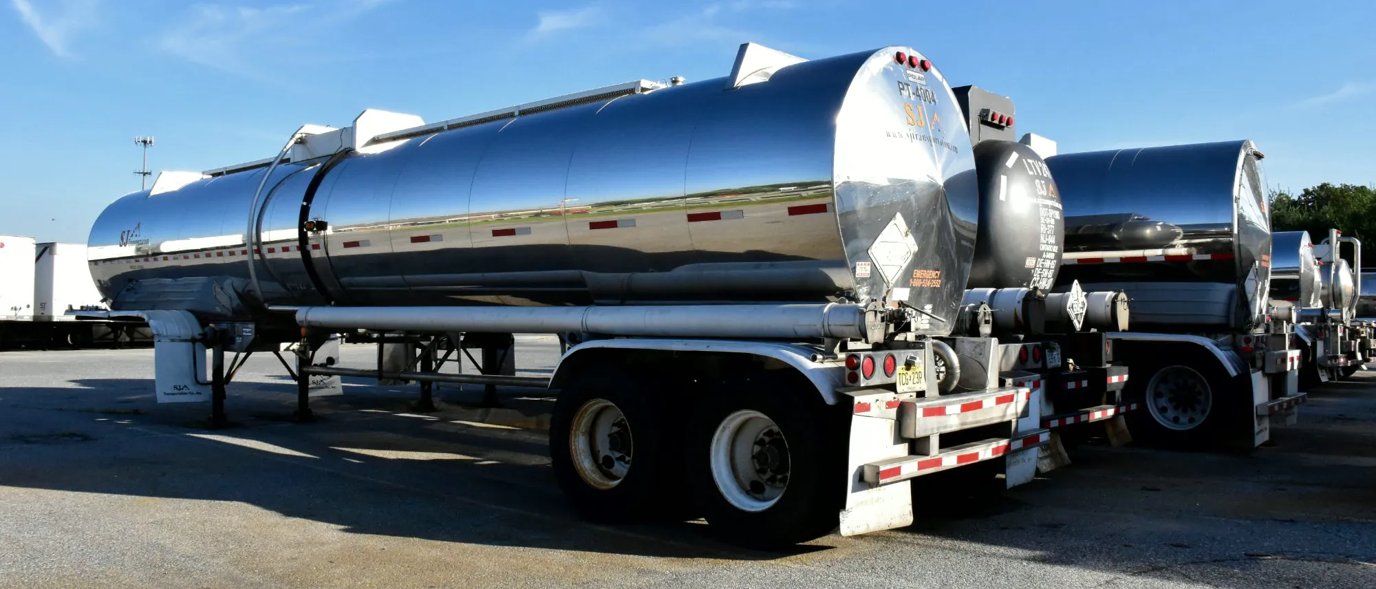 Row of polished stainless steel tank trailers parked at a carrier yard under a clear sky